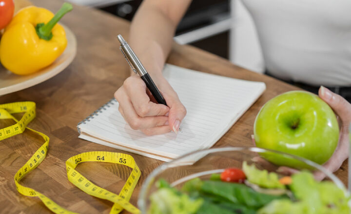 Woman writing while holding a green apple